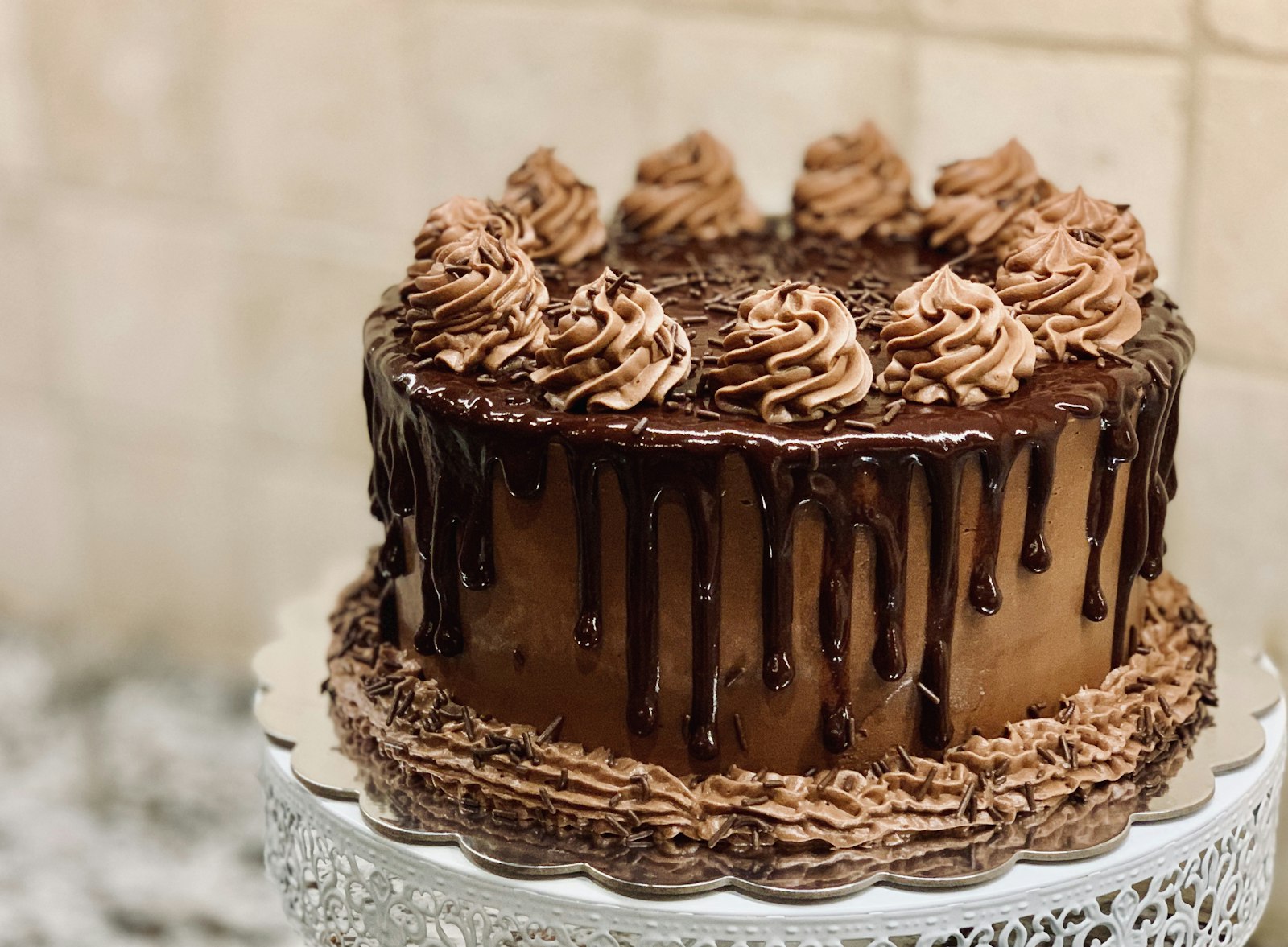 Chocolate drip celebration cake with piped rosettes on a white stand