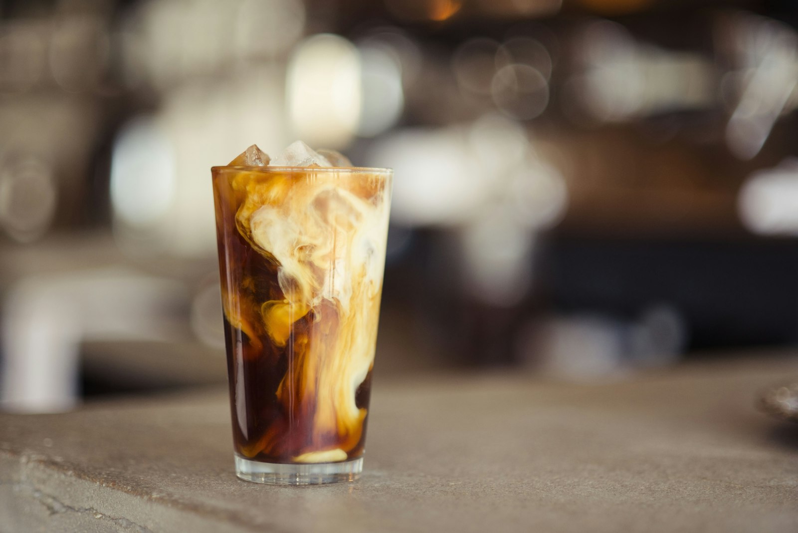 Iced latte in a tall glass with cream swirling through espresso