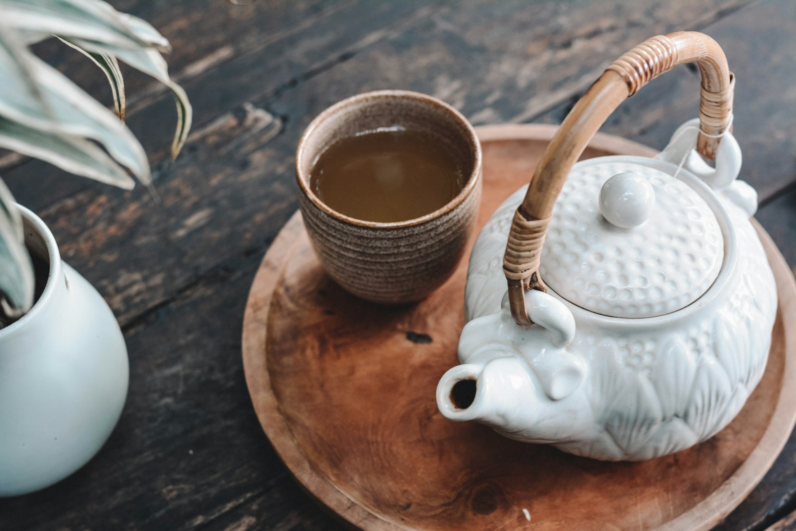 Ceramic teapot and cup of tea on a round wooden tray
